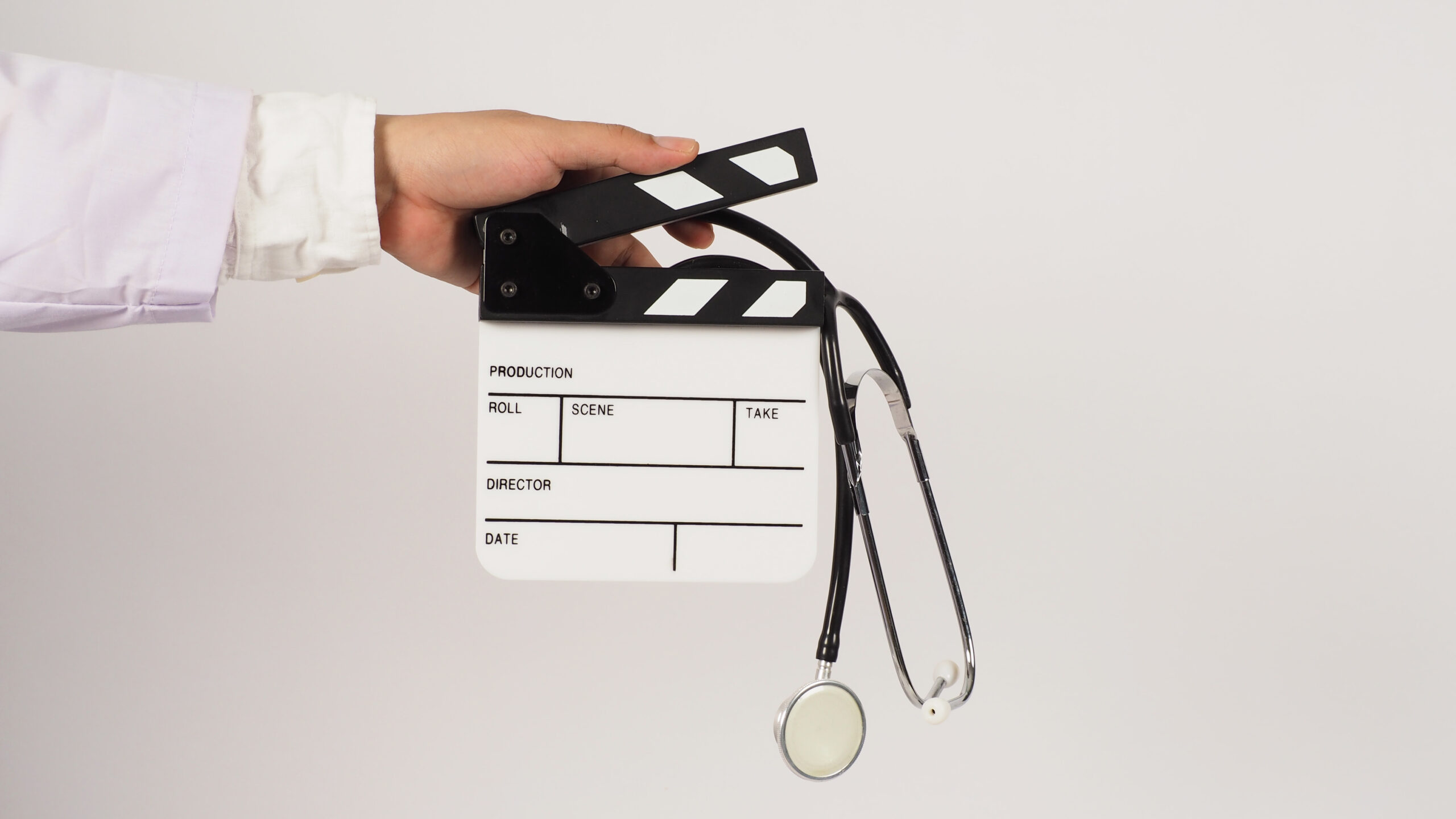 A close-up of a medical expert witness wearing a white coat holding a blank movie clapperboard and a black stethoscope, symbolizing the collaboration between healthcare professionals and the entertainment industry in film production.