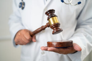 Doctor in a white coat holding a judge’s gavel, symbolizing the authority and influence of medical expert witnesses in legal cases.